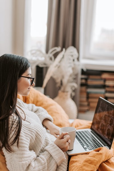 Woman wearing glasses sitting on a video call while holding a mug in her right hand.